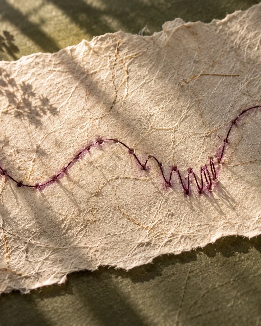 Handmade paper stitched with a plum thread in waves and tight loops, for a Chinese medicine guide to period pain and irregular cycles
